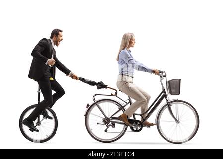 Man in a suit and tie holding an umbrella and riding a tricycle behind a woman on a bicycle isolated on white background Stock Photo