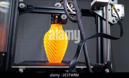 3D Printer printing a vase for home decoration with orange plastic Filament. Stock Photo