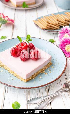 Delicious refreshing dessert, no bake sweet raspberry cheesecake bars topped with fresh berries on white rustic wooden background Stock Photo