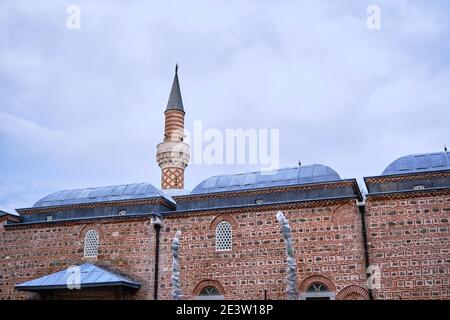 Dzhumaya Mosque in Plovdiv Bulgaria during overcast and cloudy sky background.  Roof and minaret and wall of mosque mande of red bricks. Stock Photo