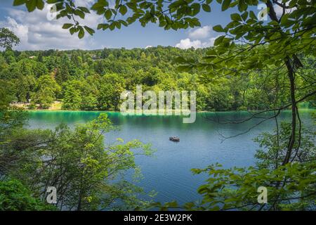 Lake and paddleboat framed by tree branches and green forest illuminated by sunlight in Plitvice Lakes National Park UNESCO World Heritage in Croatia Stock Photo