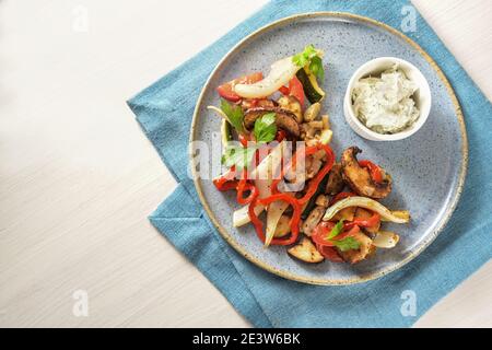 Baked oven vegetables such as bell pepper, tomato, zucchini, mushroom, fennel and eggplant with parsley garnish and a cream cheese dip on a blue plate Stock Photo