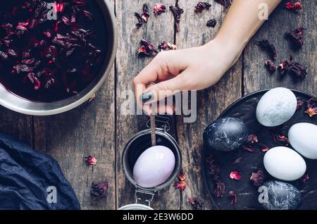Dyed Easter eggs with marble stone effect painted with natural dye carcade tea from hibiscus flowers on old wooden background. Process of dyeing eggs Stock Photo