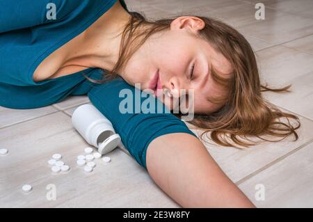 Depression woman lying on the floor at home after an overdose of pills - woman committing suicide with pills Stock Photo