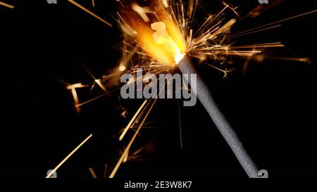 Close-up macro of burning sparklers bengal fire candle in front of black dark background. Sparkling lights at birthday party, wedding, New Year, Christmas Eve, Xmas Holidays Stock Photo