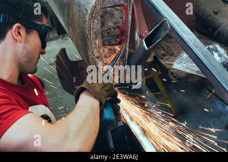 Young mechanic using angle grinder in car workshop Stock Photo