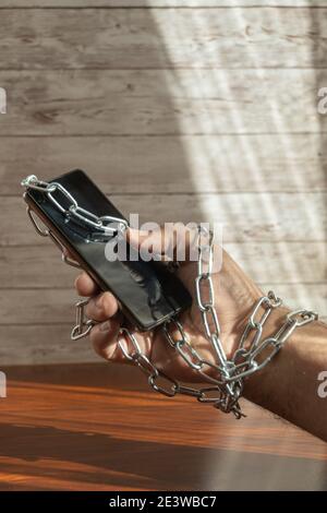 human arm using a mobile phone with iron chains with copy space in concept of slavery of the mobile and new technologies Stock Photo