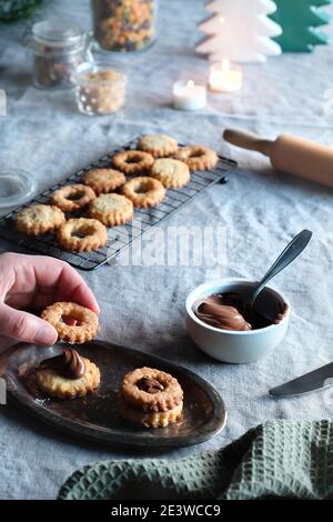 Sandwich cookies filled with hazelnut spread, nougat cream. Xmas trees, candles on linen tablecloth. Natural light.