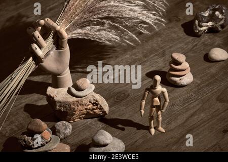 Wooden model hand holding dry withered pampas grass. Human figure with zen stone pyramids. Finding inner balance in live. Vintage, retro grunge Stock Photo