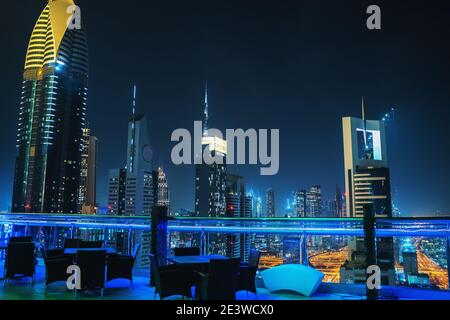 Dubai downtown night view from rooftop and empty restaurant tables on foreground, UAE, luxurious travel and tourism.