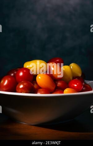 Yellow, Red, Orange Cherry Tomatoes in white bowl on wood table Stock Photo