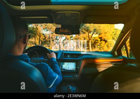 Young man driving car at summer day on a country road at sunset. Man using navigation system while driving a car Stock Photo