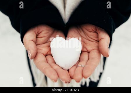 Snow heart snowball in girl gloved hands. Blurred background Stock Photo
