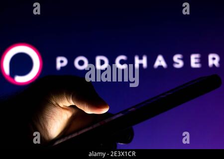 In this photo illustration, a hand of a person holds a smartphone with a Podchaser logo displayed in the background. Stock Photo