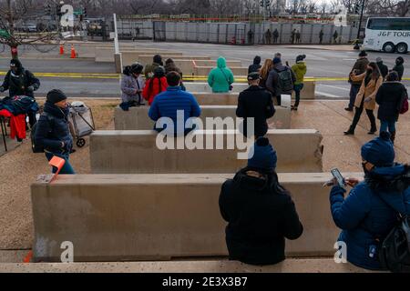 Washington, District of Columbua, USA. 20th Jan, 2021. A small crowd sits on concrete barriers as they wait for the inauguration of President Joe Biden and Vice President Kamala Harris to begin. Many people watched the ceremony on their phones because there was no public access to the National Mall in the wake of the storming of the Capitol by a pro-Trump mob just weeks before. Credit: Jungho Kim/ZUMA Wire/Alamy Live News Stock Photo