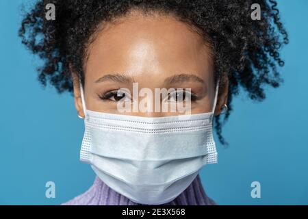 afro young woman with curly hair looking at camera wears protective medical mask being on quarantine Stock Photo