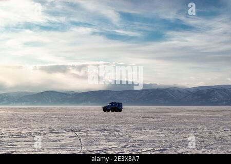 The car drives on the snow-covered ice of Lake Baikal against the background of mountains. The concept of off-road travel in extreme conditions. Stock Photo