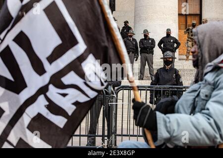 Black Lives Matter supporter holds BLM flag in front of State Troopers on the steps of the Ohio Statehouse. Activist groups in Columbus came together to form the 'United Front Against the Far-Right and Capitalist System!' This demonstration began at Columbus City Hall, marched to the Columbus Statehouse and concluded with a march back to Columbus City Hall. Left wing activist groups organized this event, because they felt they needed to make their presence known to the Far-Right after supporters of the previous president, Donald J. Trump, breached the Capitol of the United States on Jan. 6, 2 Stock Photo