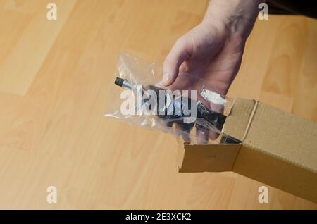 Continuous light photographic equipment, softbox. A hand pulls a new black softbox tripod in clear packaging out of a cardboard box. Stock Photo