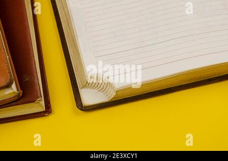 Close-up of old diaries on yellow background. Two closed diaries and one open one with the special corners torn off at the bottom of the pages. Stock Photo