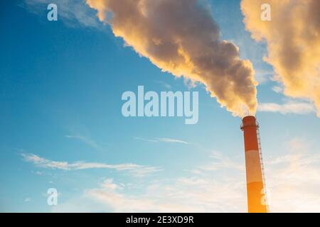 Toxic smoke from a tall red white brick industrial chimney against a blue clear sky - boiler room heats water - ecology of the earth Stock Photo
