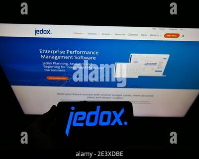 Person holding smartphone with logo of German software development company Jedox on display in front of website. Focus on mobile phone screen. Stock Photo