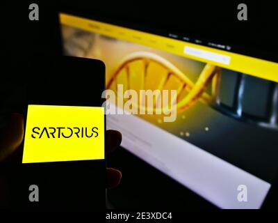 Person holding cellphone with company logo of German pharmaceutical and laboratory equipment supplier Sartorius AG. Focus on smartphone screen. Stock Photo