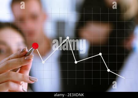 A group of people examines the financial statistics of an enterprise pointing with a hand with a pen on the graph point Stock Photo