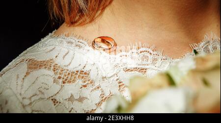 A pair of wedding rings of the bride and groom on the shoulder of the future wife in a white dress. Wedding accessories, ceremony, jewelry, Bridal bou Stock Photo