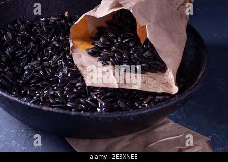 sunflower seeds in a paper craft bag and in a black charred cast iron frying pan with a handle on a gray concrete table in a dark key, rustic Stock Photo