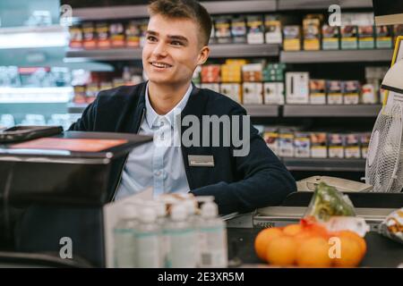 Man working at cash counter of a supermarket. Teenage cashier working at grocery store checkout. Stock Photo