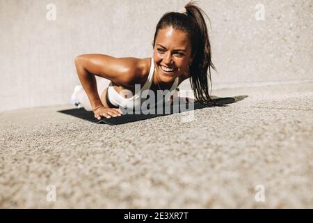 Woman doing push ups on exercise mat. Female in sportswear smiling during her workout. Stock Photo