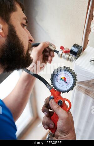 Close up of bearded man filling pipes with pressurized air to inspect for leaks in new installation. Worker using manometer, checking gas tightness of heating system. Concept of gas tightness testing. Stock Photo