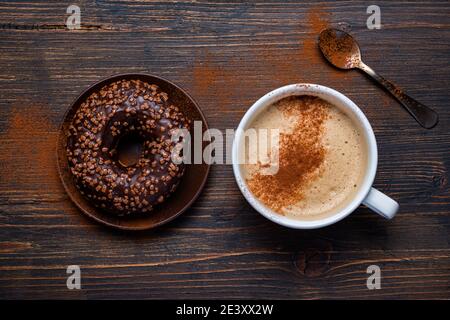 on the rustic wooden background, delicious breakfast with cappuccino and chocolate glazed donuts Stock Photo