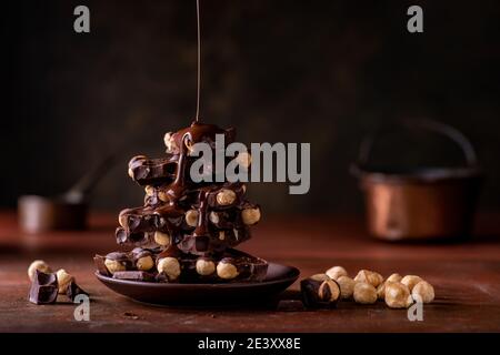 melted chocolate poured on overlapping pieces of dark chocolate with hazelnuts Still life Stock Photo