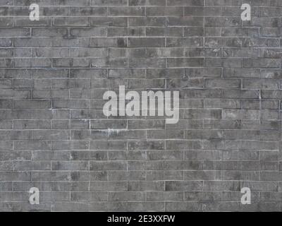 A gray brick wall with dark and light spots of dirt and smudges. Stock Photo