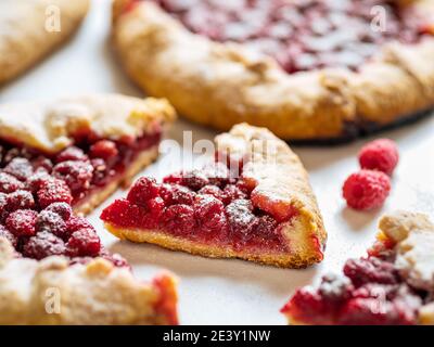 Slice of perfect raspberry galette. Delicious rustic homemade tart with frozen or fresh raspberries on white marble background. Beautiful piece of galette with raspberries, copy space Stock Photo