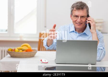 Smiling businessman working in home office talking on smart phone in front of laptop - focus on the face Stock Photo