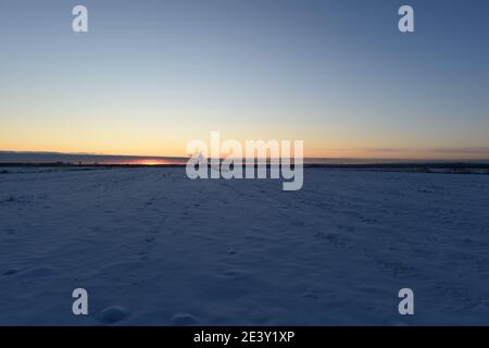 Sunset on the horizon over a snowy field Stock Photo
