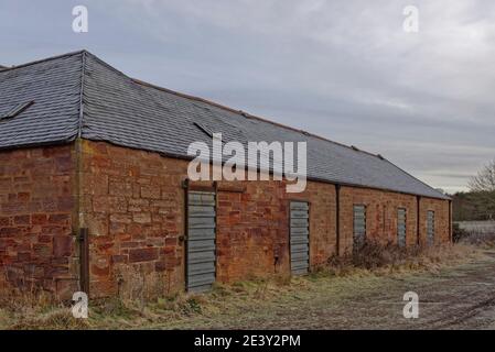 Part of an old Agricultural Farm Store Complex with metal shutter doors built into the red Stone Building on an abandoned Golf Course near Arbroath. Stock Photo