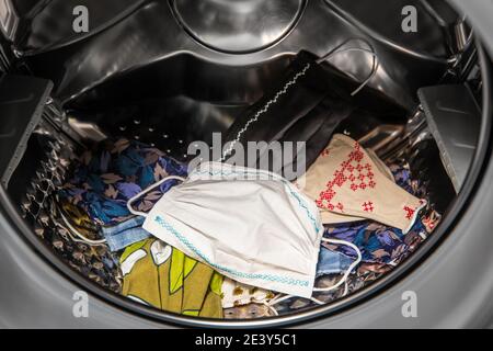 Lot of homemade textile reusable protective face masks inside washing machine, ready to wash. Home indoors. Stock Photo