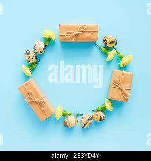 Happy easter festive circle frame. Easter layout made of quail eggs, yellow flowers and craft gift on blue background with copy space Creative Flat la Stock Photo