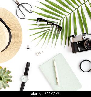 Top view home office desk. Workspace with straw hat, glasses, retro camera, notepad and tropical palm leaf on white background. Flat lay, top view. Stock Photo