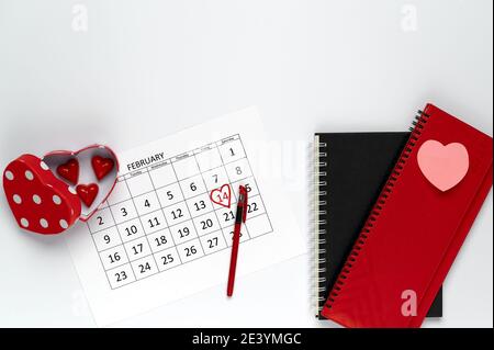 Valentine's Day in the office. Heart shaped box of chocolates, February calendar and notebooks on a white table. Stock Photo