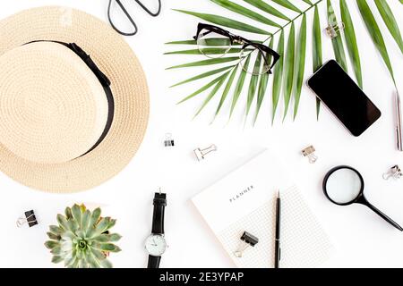 Top view home office desk. Workspace with straw hat, glasses, retro camera, notepad and tropical palm leaf on white background. Flat lay, top view. Stock Photo