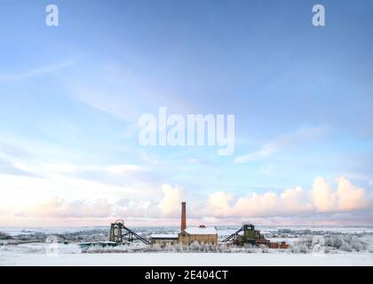 Old abandoned national coal board mine in countryside with industry engine house winding wheel snowfall Christmas winter snow scene landscape Pleasley Stock Photo