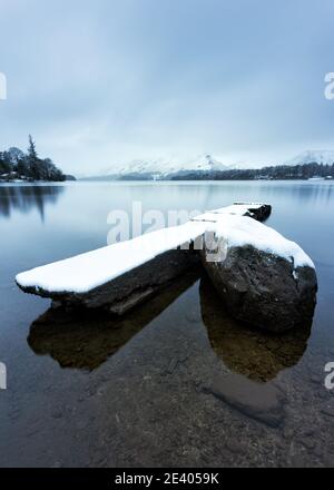 Old concrete jetty covered in a layer of white snow on a calm Winter morning by Derwentwater in the Lake District, UK. Stock Photo