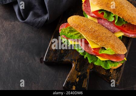 Healthy sandwiches with bran bread, cheese, green lettuce, tomato and sliced salami on rustic wooden stand. Breakfast concept. Top view. Stock Photo
