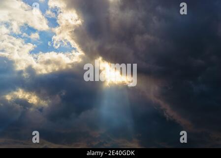 San ray breaks through the gap in a large dark cloud covering the blue sky. Changing weather from clear sunny to rainy overcast. Dramatic cloudscape. Stock Photo