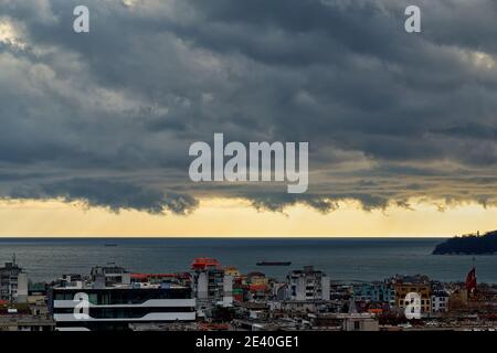 Dramatic landscape of stormy sky over small seaside city. The sky turned yellow before the storm. Dark nimbostratus clouds hang over town and sea. Stock Photo